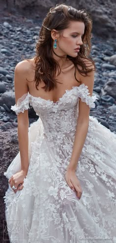 a woman in a wedding dress is standing on the rocky ground with her hands behind her back