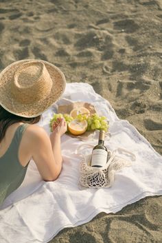 a woman is sitting on the beach with a bottle of wine and grapes in her hand