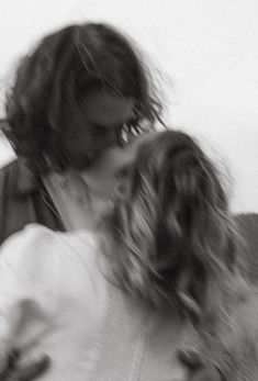 a man and woman kissing each other in front of a white background with blurry hair