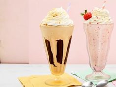 two drinks with whipped cream and strawberries on the top are sitting next to each other