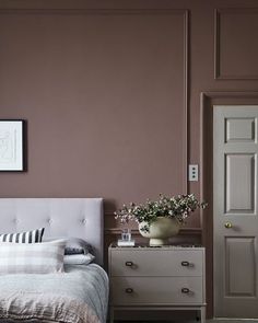 a white bed sitting next to a dresser with a vase on it's headboard