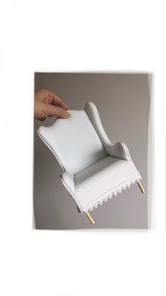 the chair is made out of white paper and has a hand holding it up to its back