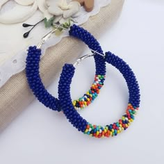 two pairs of beaded hoop earrings sitting on top of a piece of fabric next to a flower