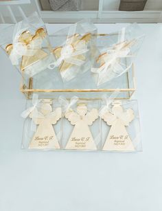 four wooden angel ornaments in clear boxes on a white counter top with ribbon around the edges