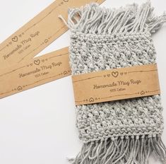 two tags are attached to the back of a gray knitted scarf on a white surface