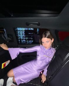 a woman sitting in the back seat of a car wearing a purple dress and heels