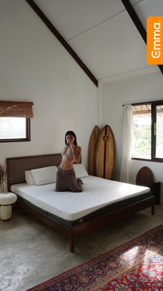 a woman sitting on top of a bed next to a surfboard in a room