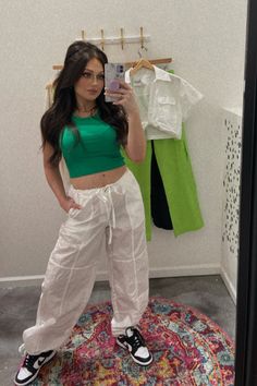 Mirror selfie featuring a fashion-forward outfit consisting of white cargo pants and a green tank top. The person is standing in front of a mirror, posing confidently while showcasing the trendy ensemble. The white cargo pants are loose-fitting with multiple pockets, paired with a green tank top that has a relaxed fit. The outfit exudes effortless chic, perfect for a casual day out or a springtime fashion statement. Sporty Summer Cargo Pants With Pockets, Sporty Summer Cargo Pants With Drawstring, Sporty Summer Cargo Pants With Cargo Pockets, Green Sporty Summer Cargo Pants, Casual Summer Cargo Parachute Pants, Green Sporty Parachute Pants For Summer, Summer Parachute Pants With Drawstring, Summer Cargo Pants With Drawstring, Summer Wide Leg Cargo Pants With Drawstring