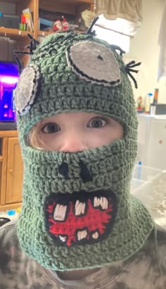 a young boy wearing a green crocheted hat with an ugly monster on it