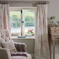 a chair sitting in front of a window next to a table with flowers on it