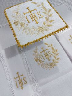 three embroidered napkins with gold lettering and cross designs on them, all in different colors