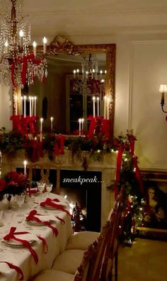 a dining room table set for christmas dinner with red ribbon on the table and candles in the fireplace