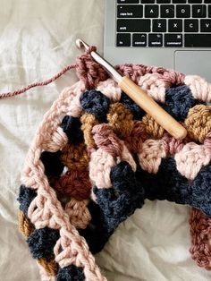 an open laptop computer sitting on top of a bed next to a crocheted scarf