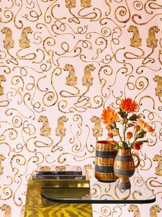 two vases with flowers on a table in front of a wallpapered background