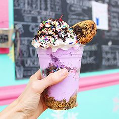 a person holding up an ice cream sundae with sprinkles and cookies