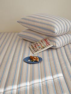 two pillows and a plate with food on it sitting on top of a striped bed spread