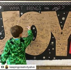 a young boy writing on a wall with the word joy written in large letters and snowflakes