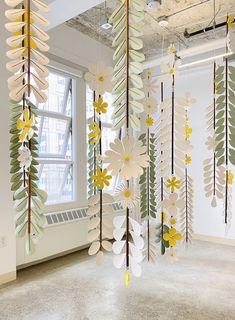 an art installation with paper flowers and leaves hanging from it's ceiling in front of a window