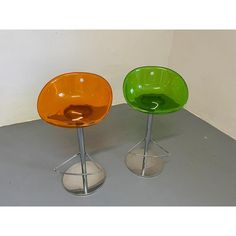 two colorful chairs sitting next to each other on top of a gray floor in front of a white wall