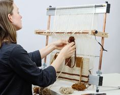 a woman working on a weaving project with yarn and wood looms in the background