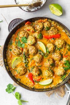 a pan filled with meatballs and vegetables on top of a white table next to rice