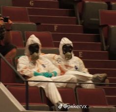 two people in gas masks sitting on the bleachers