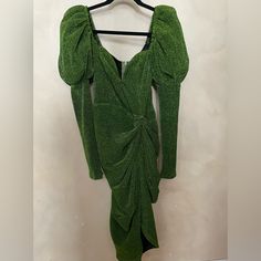 a green dress hanging on a hanger in front of a white wall with an open back and long sleeves