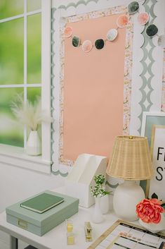 a white desk topped with a lamp next to a window and a pink sign on the wall