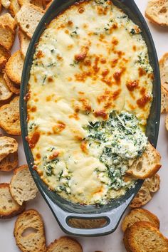 a casserole dish with spinach and cheese in it surrounded by crackers