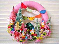 a pink wreath with gnomes and flowers hanging on the side of a house wall