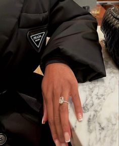 a close up of a person's hand on a marble counter top with a purse in the background