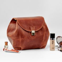 a brown leather bag sitting on top of a table next to makeup and eyeliners