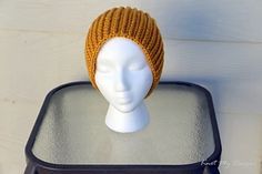 a white mannequin head wearing a yellow knitted hat on top of a black case