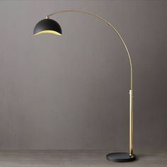 a black and gold floor lamp on a wooden table next to a gray wall with a grey background