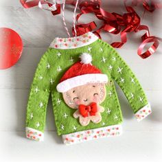 an ugly sweater ornament hanging from a red ribbon on a white wooden table