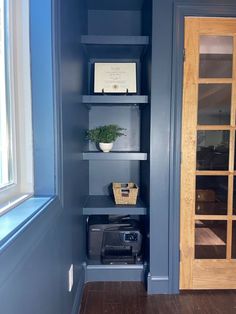 an empty shelf in the corner of a room with blue walls and wooden floors, next to a window