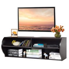 a flat screen tv sitting on top of a wooden shelf next to a vase with flowers