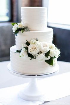 a three tiered white cake with flowers on the top and bottom is sitting on a table