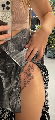 a woman with a flower tattoo on her thigh holding a cell phone and looking at the camera