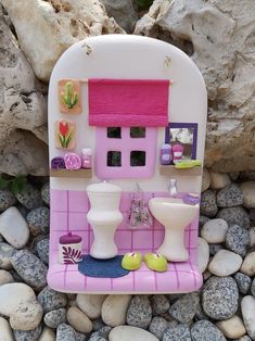 a pink and white doll house sitting on top of a pile of rocks next to a rock wall