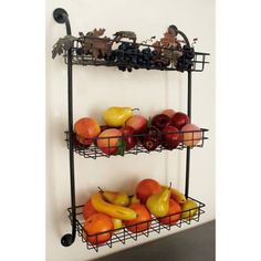 two metal racks holding fruit on top of each other in front of a white wall