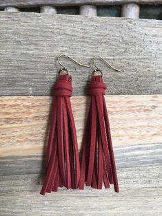 red leather tasselled earrings with brass hooks on wooden background, close up photo