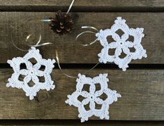 three crocheted snowflakes sitting on top of a wooden table next to a pine cone