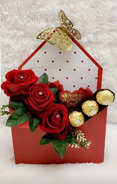 a red box filled with chocolates and roses on top of a white furnishing