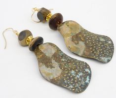 1 Pair Available! Pics do not do justice....long wavy handforged brass drops have been textured with hammer and patinated.  Raised dots are brushed to reveal shiny gold metal..  The colors are subtle....a little speck of blue, some golden tan, gray-blue, dark brownlovely patterns created by patination.  I have topped the statement sized drops with stack of handcarved horn beads separated by GP  bead. Earrings are a tad over 3 1/2 inches in length, including my handmade 14KT GF French wires.  Lig Artisan Brass Earrings With Patina, Rustic Gold Brass Earrings, Earthy Bronze Brass Earrings, Rustic Gold Drop Earrings, Hand Forged Brass Earrings In Brown, Rustic Brass Earrings With Patina, Rustic Gold Dangle Jewelry, Rustic Gold Metal Earrings, Golden Tan