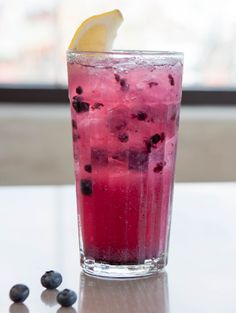 a glass filled with blueberries and lemon on top of a table next to a window