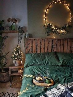 a bed with green sheets and lights on the headboard is decorated with greenery