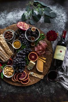 an assortment of cheeses, meats and fruit on a wooden platter next to a bottle of wine