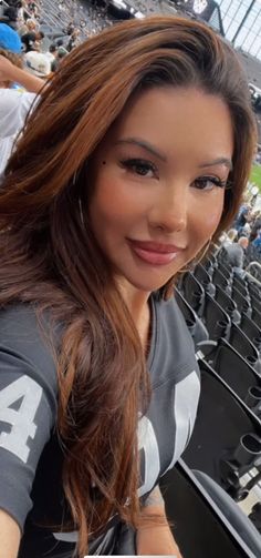 a woman with long hair sitting in the stands at a baseball game wearing a gray shirt