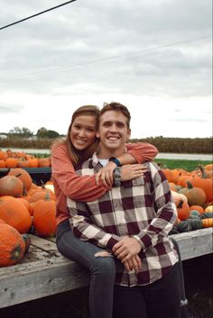 a man and woman sitting on top of a truck filled with pumpkins